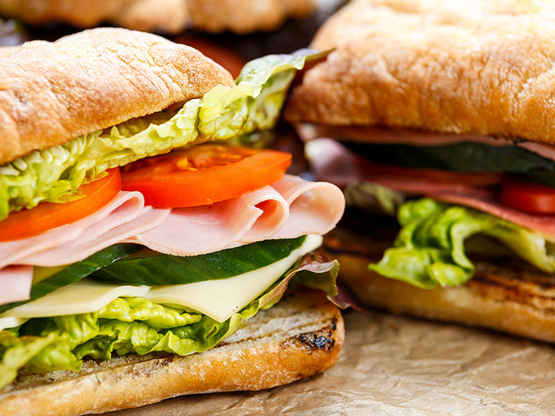 Freshly made sandwich with ham, tomatoes, cucumbers, cheese and lettuce on an office desk